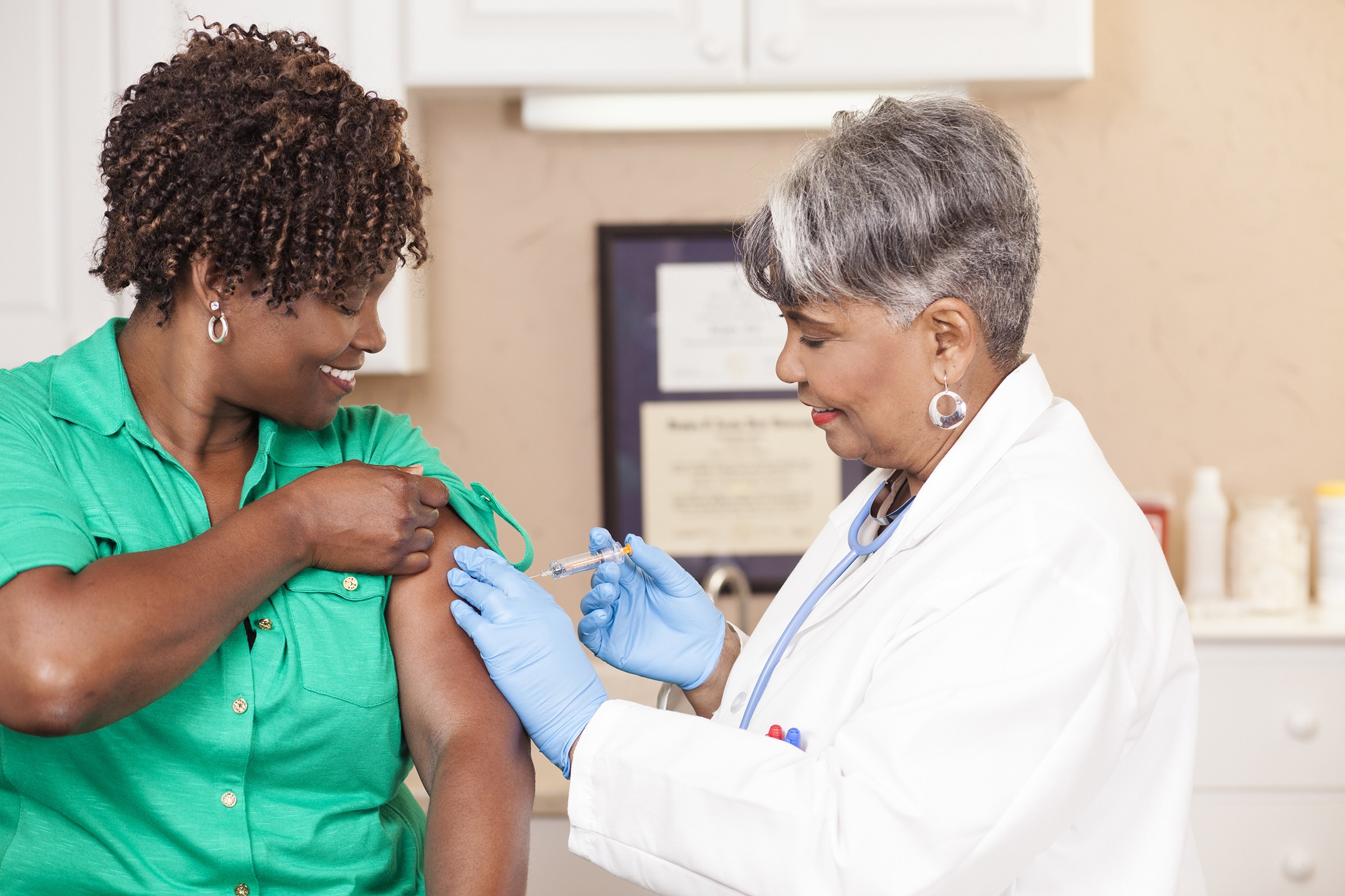 年长医生或护士在当地医疗诊所、医院或医生诊所，为非裔、中成年患者提供流感疫苗。注意：这是工作室拍摄的照片，而非实际的医疗诊所。