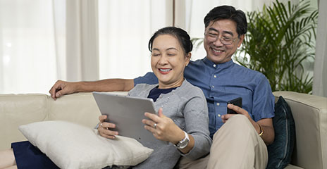 一对亚裔夫妇微笑着坐在沙发上看电脑