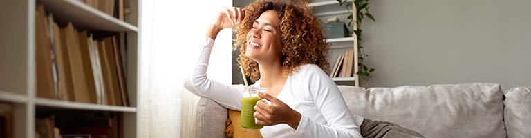 mindful woman smiling and drinking green juice and looking out the window