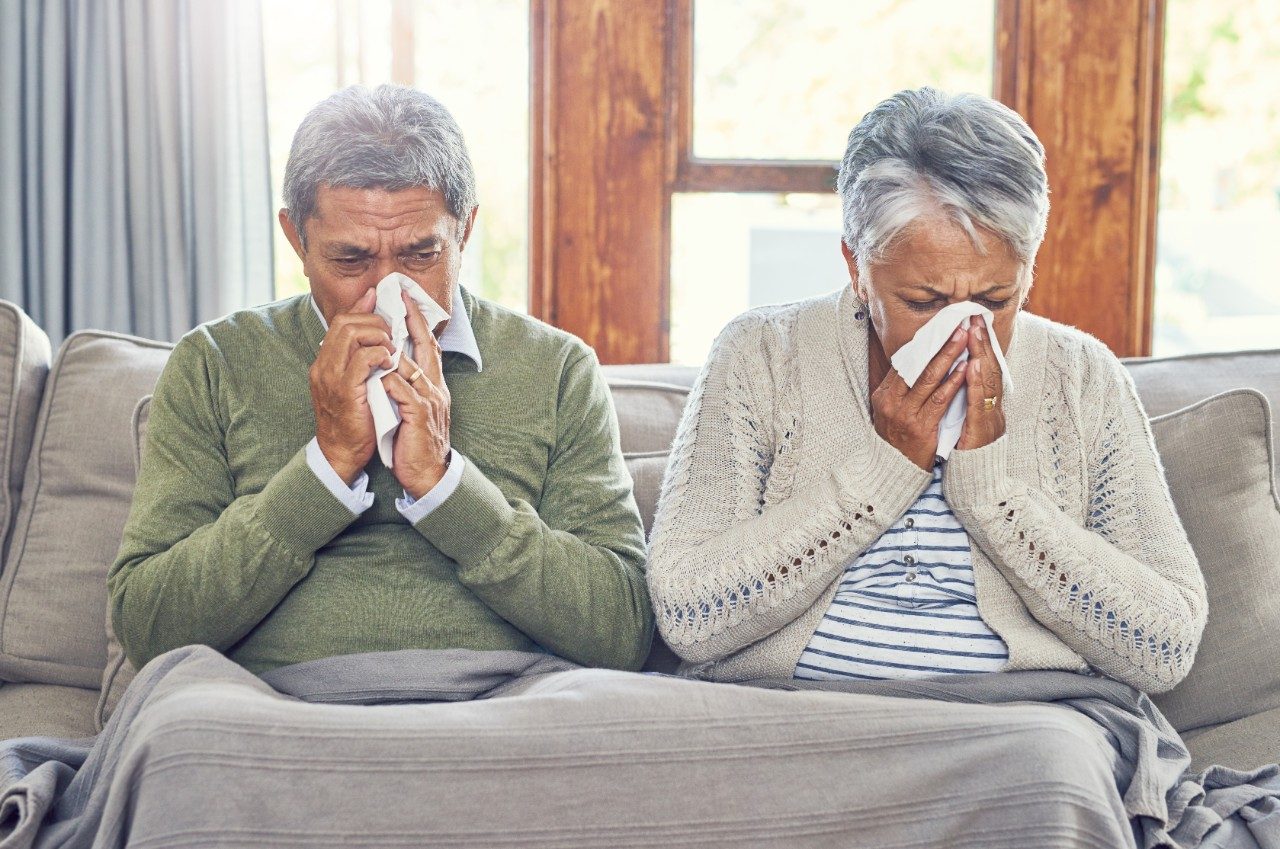 照片中，一对病重的老年夫妇坐在家里的沙发上，每人用纸巾擤鼻涕