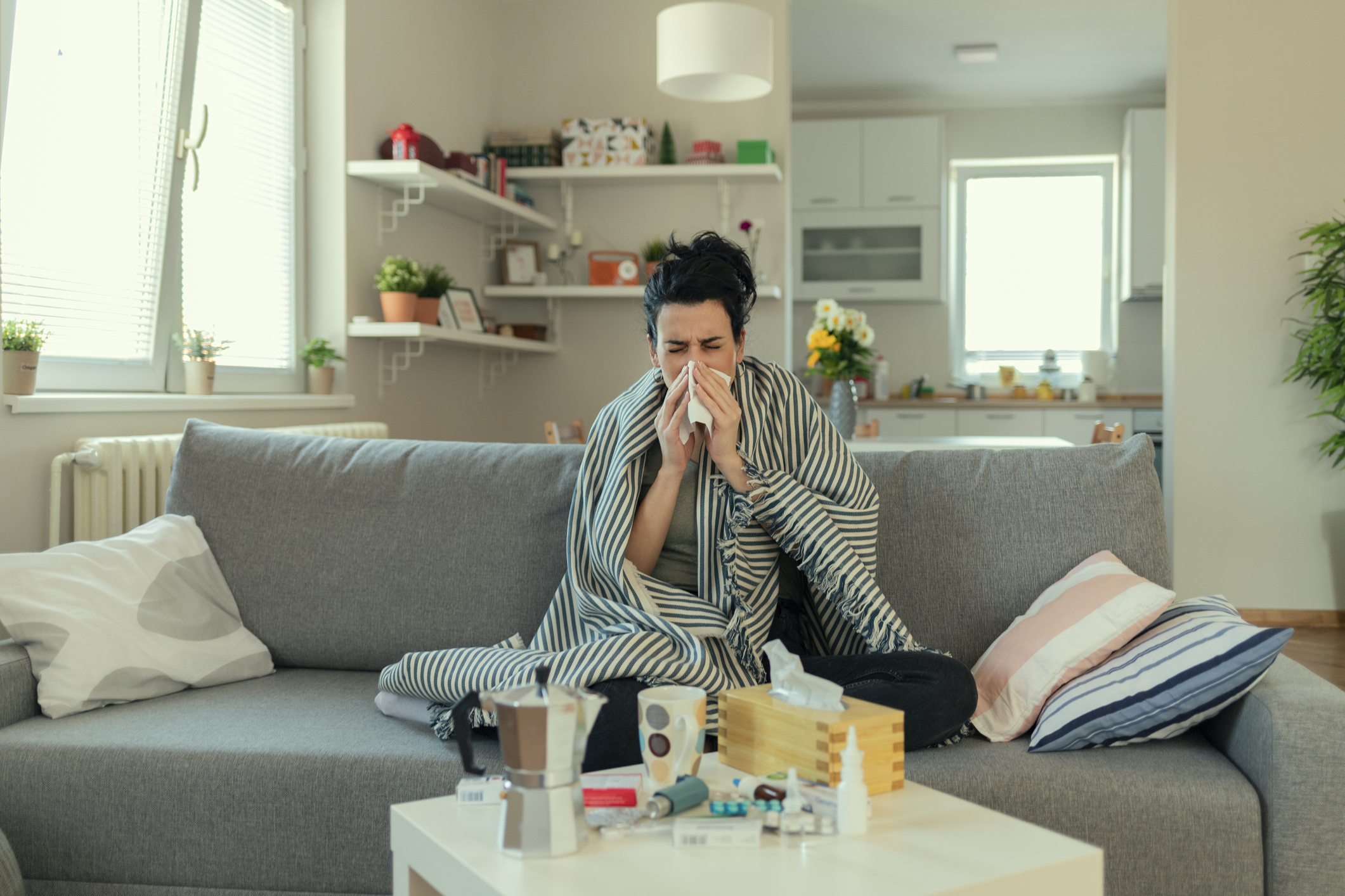 一名患流感高烧的女性，盖着毯子躺着，在客厅休息。她精疲力竭，还遭受流感折磨。一个流鼻涕的生病的女性躺在床上。一个患感冒的女孩在沙发上躺着，用纸巾擤鼻涕