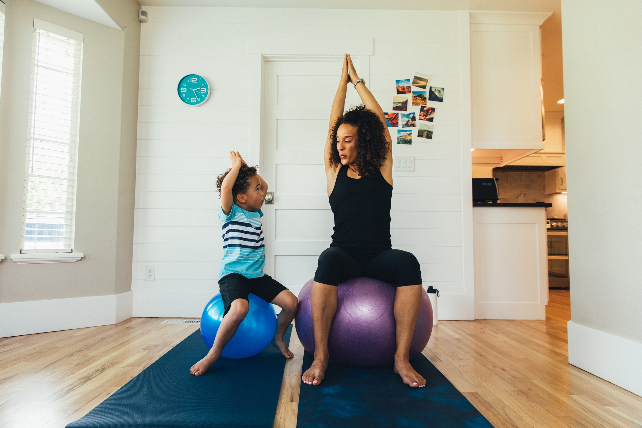 一位母亲在家里和她幼小的儿子在健身球上锻炼。她正在通过适当的拉伸和锻炼来教男孩健康生活方式的重要性。