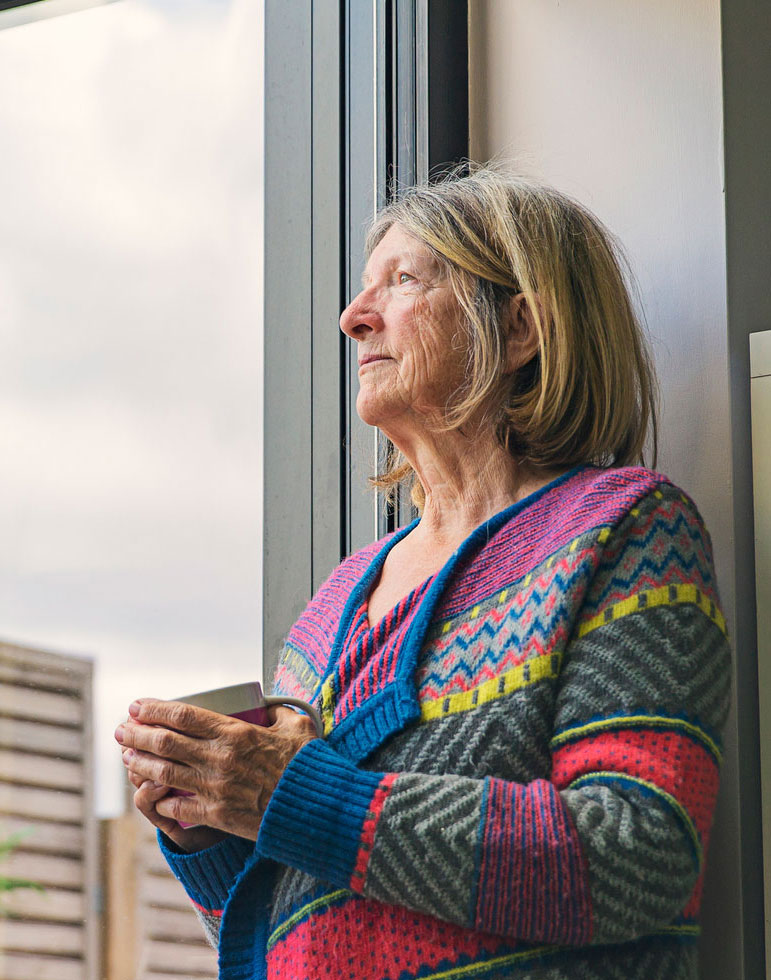 Elderly woman looking outside the windows of New York City while drinking coffee.