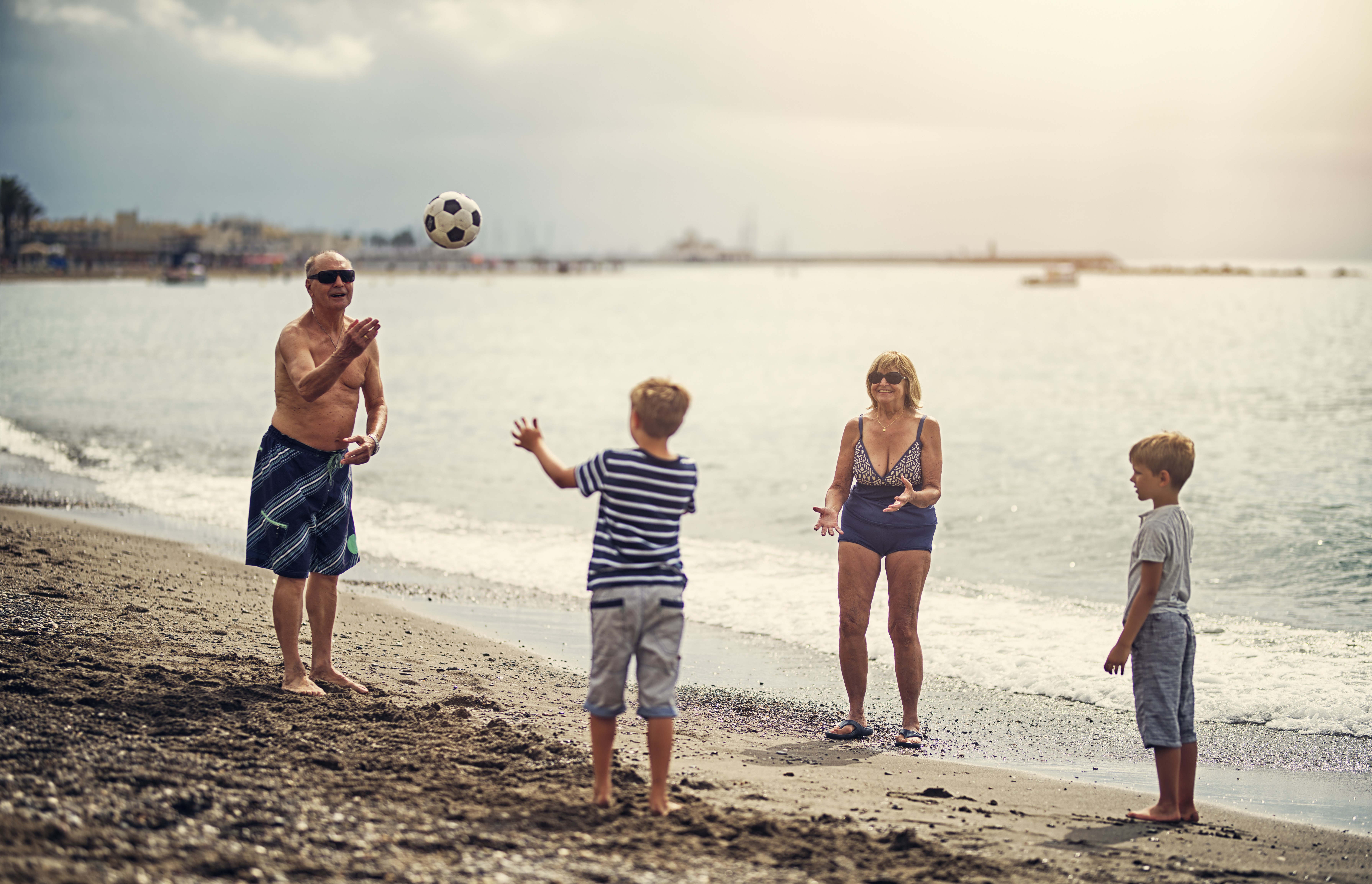 小男孩们和他们的祖母和祖父一起玩接球。男孩们 7 岁了。一家人在沙滩上享受阳光灿烂的夏日。