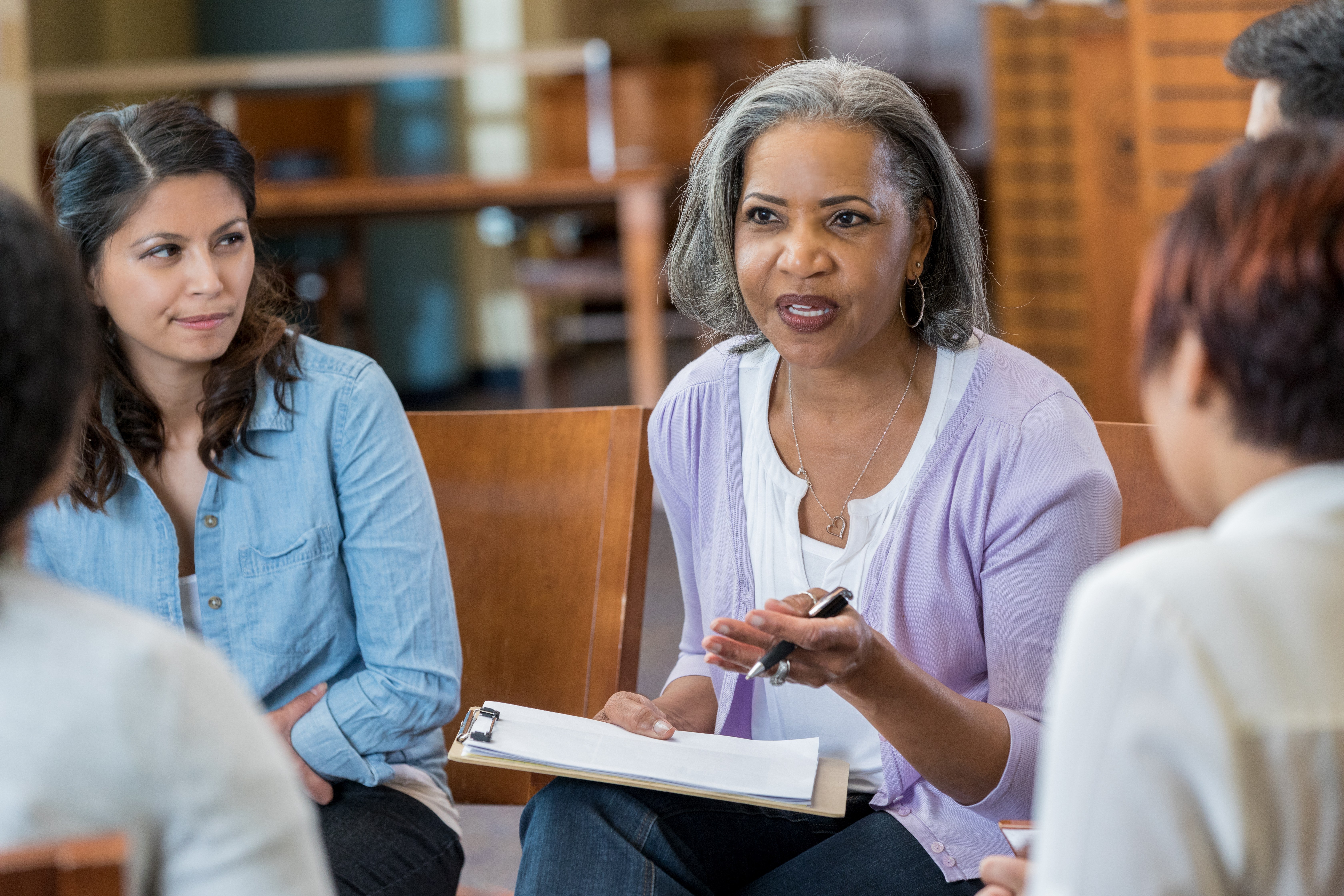 在支持小组或小组治疗会议上与客户交谈时，严肃的非洲裔美国女性心理健康职业手势。她拿着一个剪贴板。