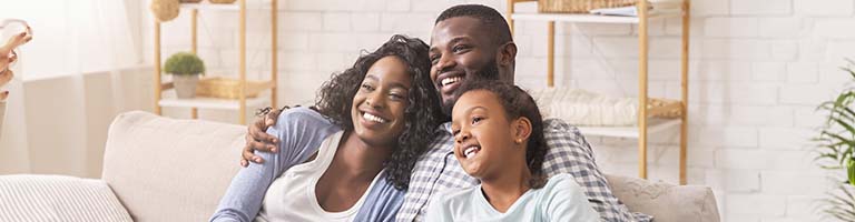 father, mother and daughter watching tv together, relaxing at home.