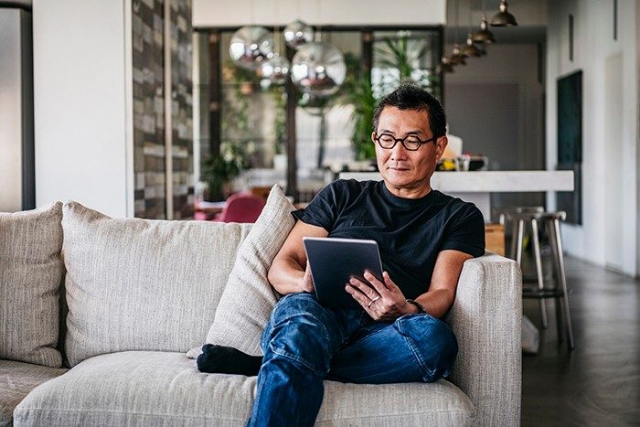 一个 50 多岁的中国男性在家里的沙发上休息，他穿着休闲衣服，看电子书、上网